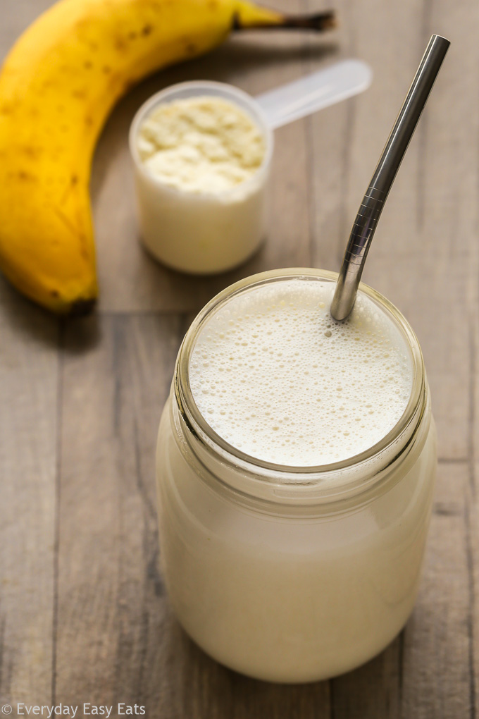 Overhead view of a Vanilla Protein Shake in a glass jar with a metal straw on a wooden background.