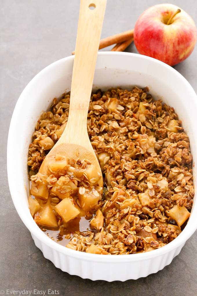 Overhead view of Healthy Apple Crisp in a large white serving dish with a wooden spoon taking a spoonful out.