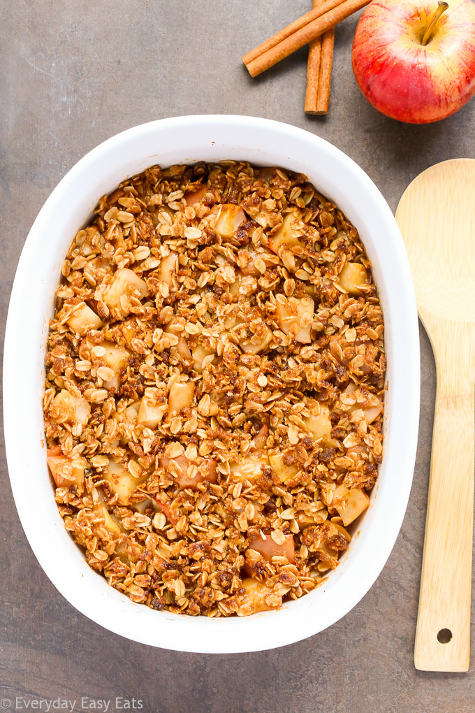 Overhead view of Healthy Apple Crisp in a large white serving dish with a wooden spoon beside of the dish.